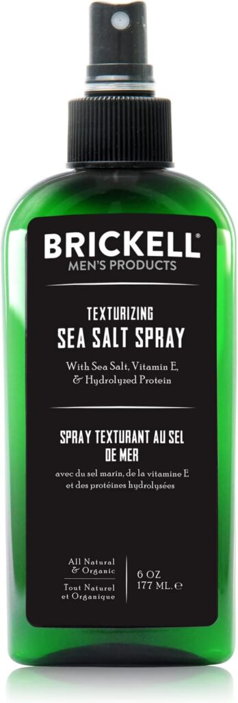 Close-up of a green bottle of Brickell Men's Texturizing Sea Salt Spray, labeled with key ingredients like sea salt, vitamin E, and hydrolyzed protein, 6 oz