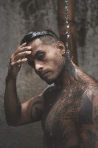 Moody portrait of a tattooed man under a waterfall, exuding strength and confidence.