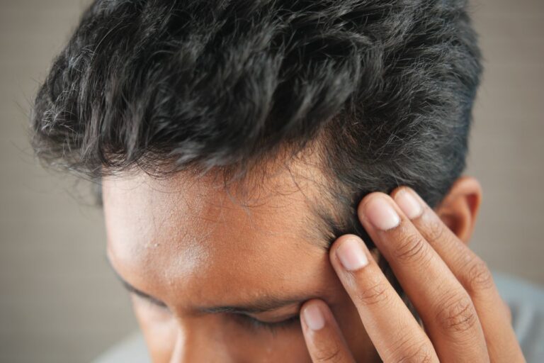 Close-up of a man's hand touching his head in contemplation. Neutral tones and soft lighting.