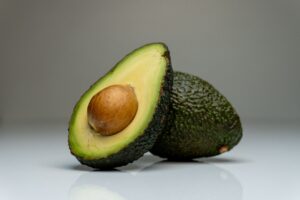 Close-up of a halved avocado with seed, showcasing vibrant colors on a reflective white background.