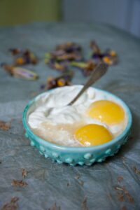 A rustic turquoise bowl containing eggs and yogurt on a textured surface.