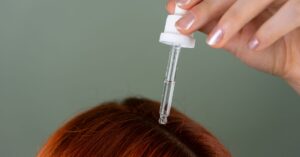 Close-up of applying serum to roots with a precision dropper on red hair, showcasing hair care routine.