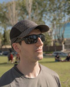 Man wearing sunglasses and cap, enjoying a sunny day outdoors in a park.