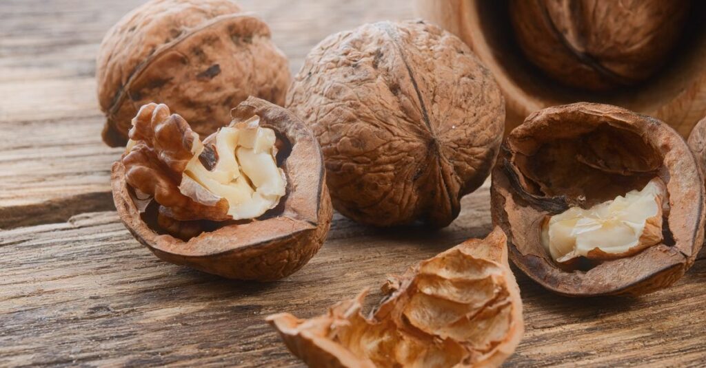 pexels-photo-35318132-35318132 Close-up of walnuts, both whole and shelled, on a rustic wooden table, showcasing natural textures.