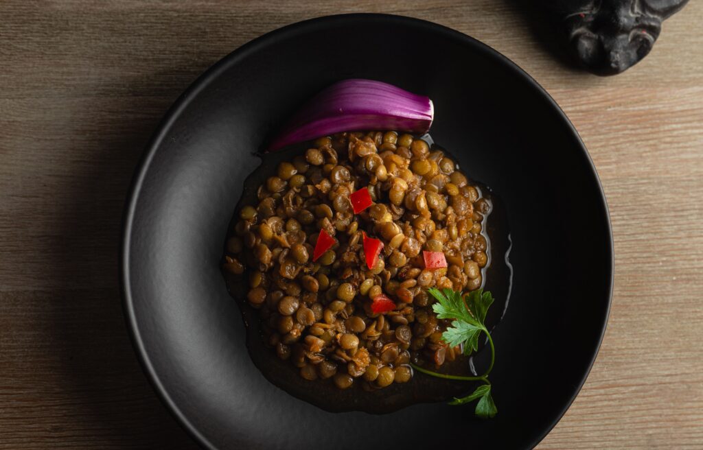 pexels-photo-35763746-35763746 Top view of a savory lentil dish garnished with onion and parsley in a black bowl.