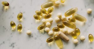 A variety of capsules and pills scattered on a light marble background.