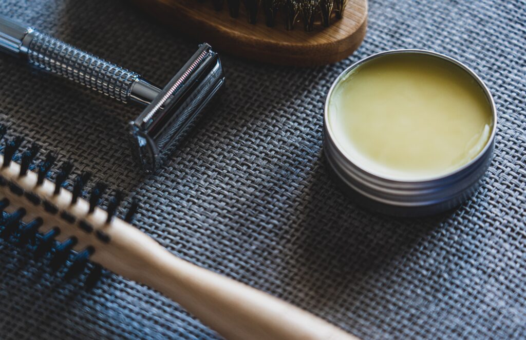 pexels-photo-3944792-3944792 A flat lay of grooming tools including a razor, brush, and pomade on a textured surface.