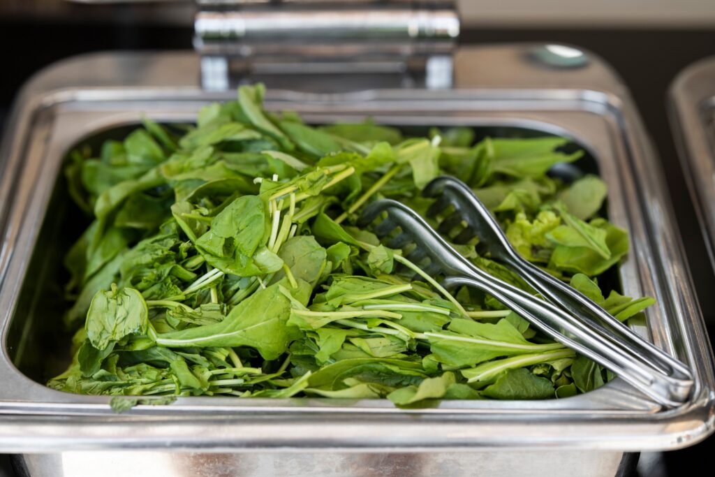 pexels-photo-5374415-5374415 Close-up of fresh green vegetables in a serving tray with metal tongs, ideal for healthy food concepts.