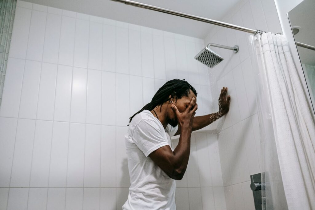 pexels-photo-5700194-5700194 Side view depressed preoccupied African American male in white shirt covering face with hand in anxiety in bathroom