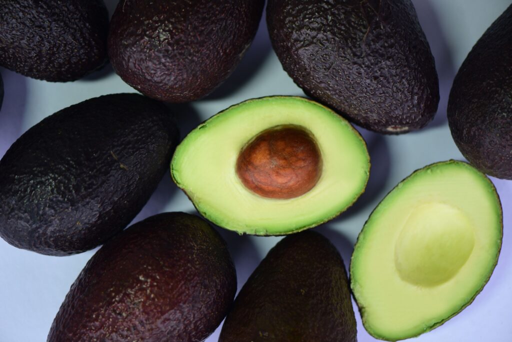 pexels-photo-5785658-5785658 Top view of fresh avocados and cut halves on a white surface, showcasing their vibrant green color.