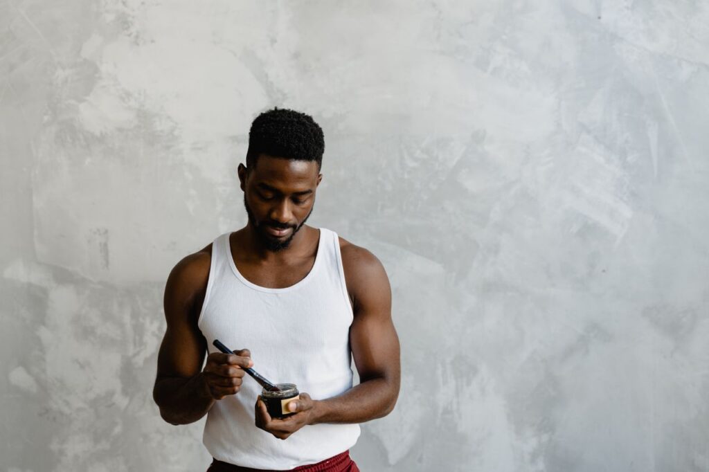 A man in a self-care routine applies a facial mask with a brush, embracing skincare.