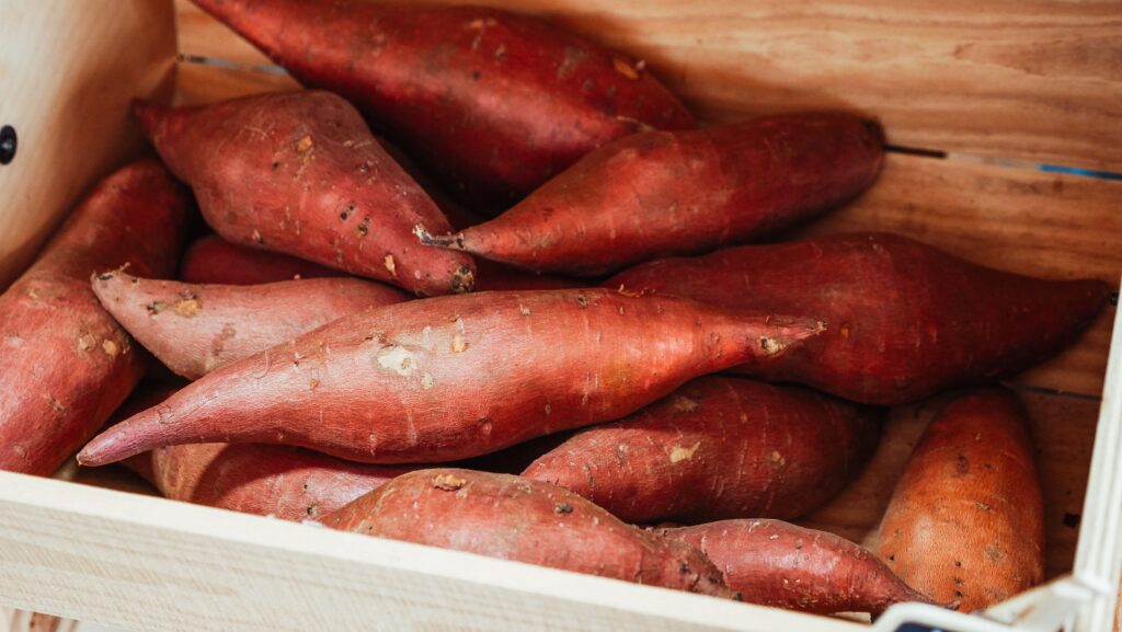 pexels-photo-7456548-7456548 Close-up of fresh sweet potatoes in a wooden crate, ideal for cooking.
