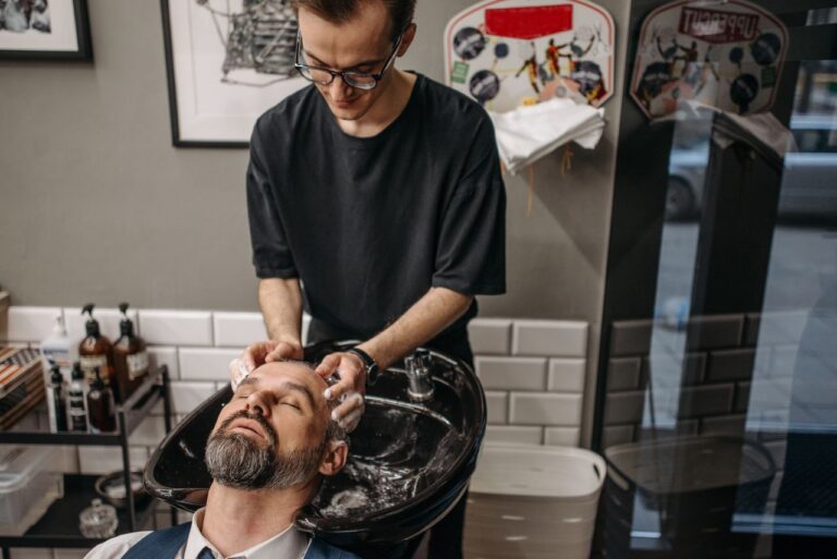 Barber washing client's hair at shampoo station in modern salon setting.