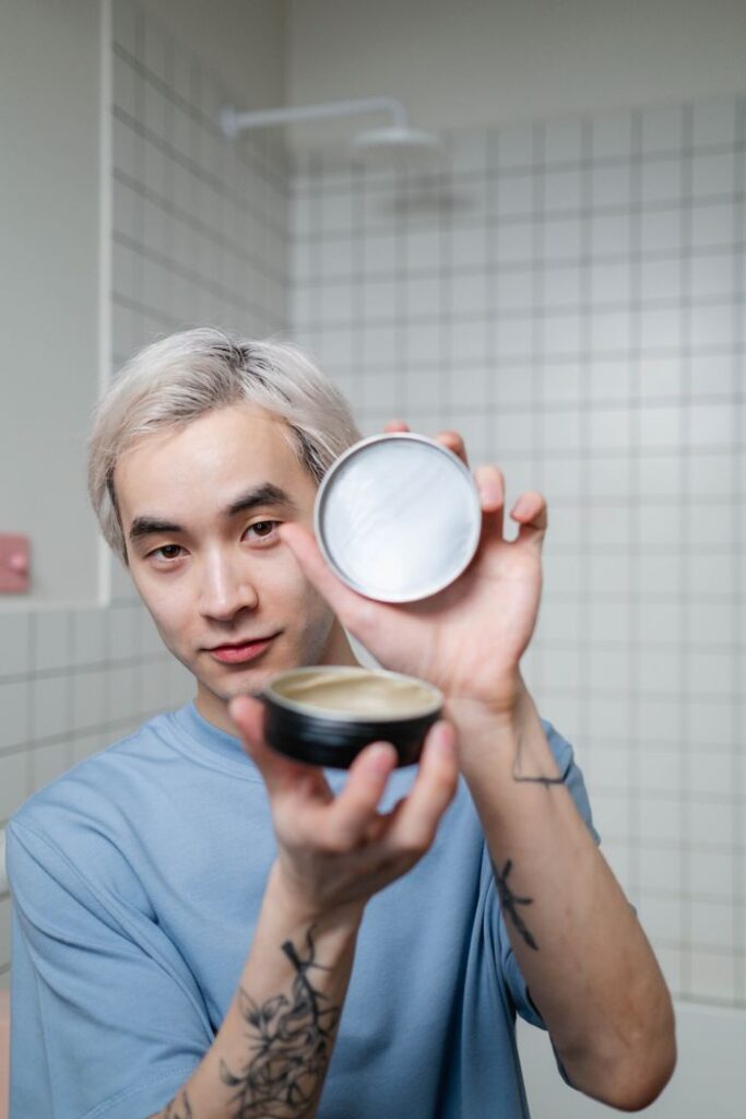 pexels-photo-8160474-8160474 A young man with blonde hair shows off a hairstyling product in a modern bathroom.
