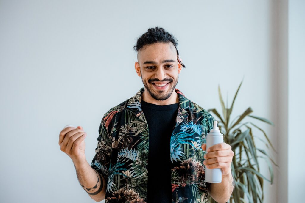 pexels-photo-8360443-8360443 Portrait of a man smiling and holding a can, wearing a colorful patterned shirt indoors.