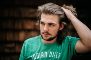 Casual portrait of a man with long brown hair wearing a green t-shirt, hand on hair.