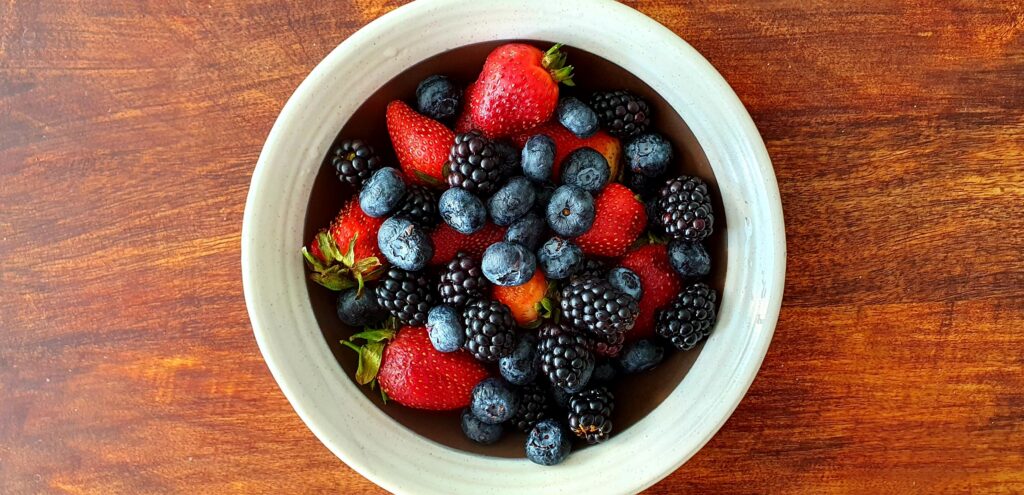 pexels-photo-9285704-9285704 A vibrant assortment of strawberries, blackberries, and blueberries in a bowl on a wooden surface.