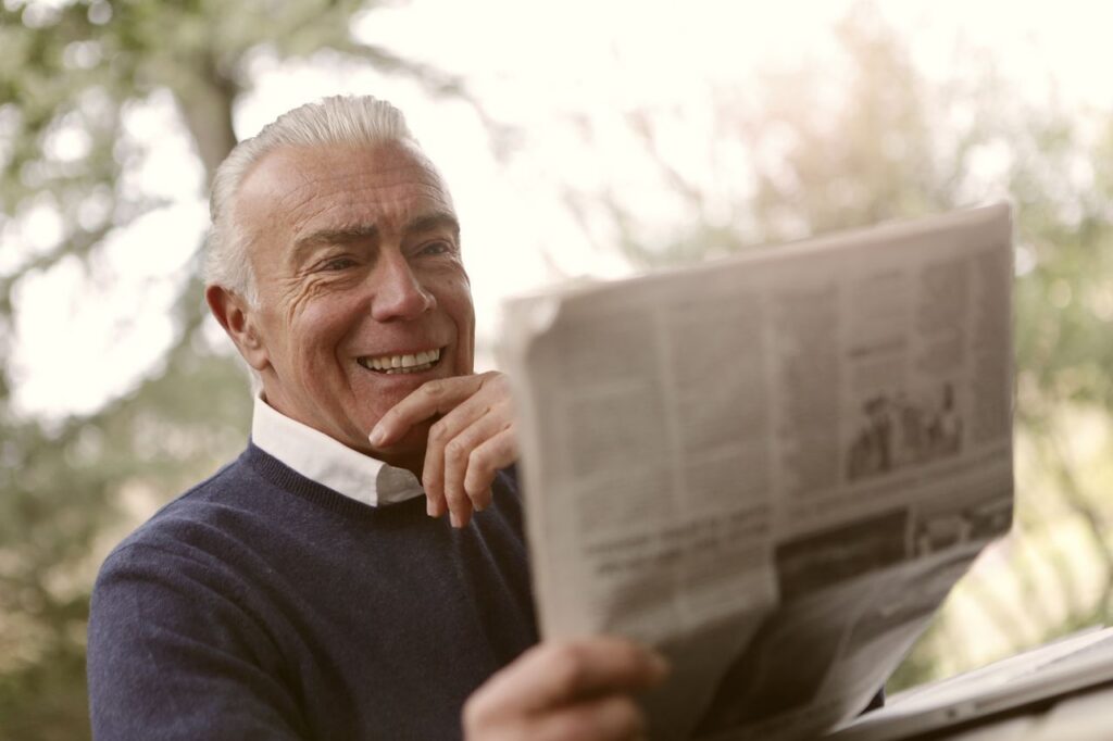 Smiling senior man reading a newspaper outdoors in a relaxed atmosphere.
