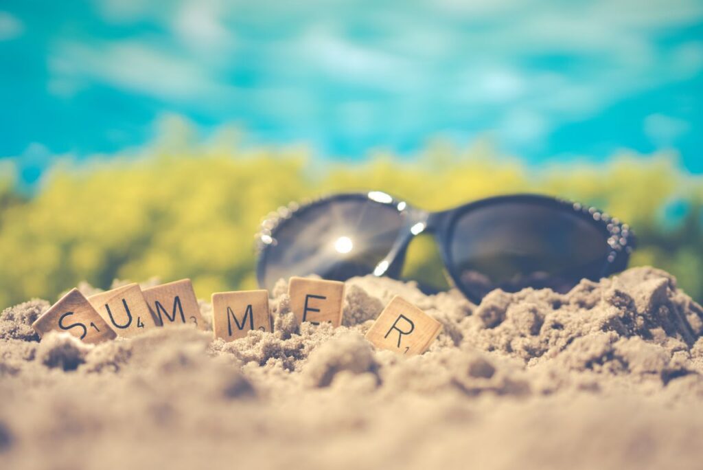 Sandy beach scene with sunglasses and 'summer' spelled in letter tiles, capturing vacation vibes.