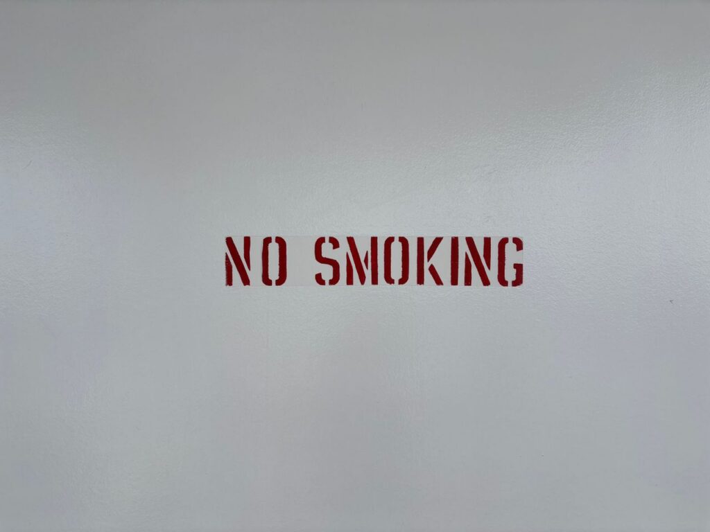 Simple 'No Smoking' sign stenciled on a blank grey wall, promoting a smoke-free environment.