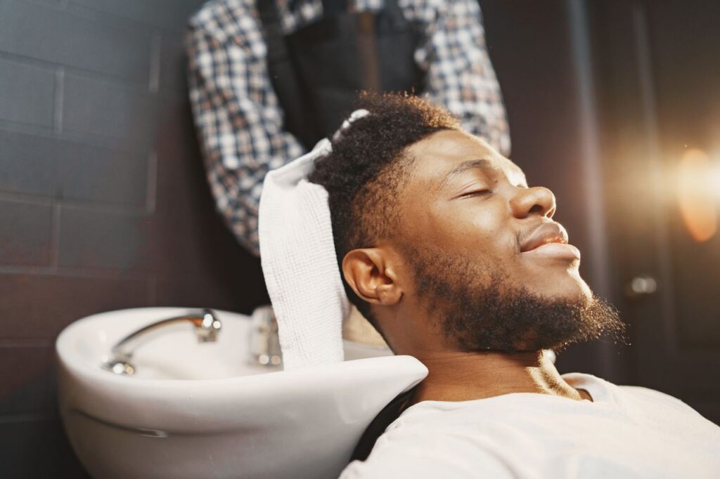 pexels-photo-7447131-7447131 A man enjoying a hair wash with his eyes closed, experiencing relaxation at a barber shop.